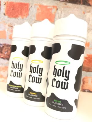 Holy Cow bottles displayed on a white shelf in front of a brick background