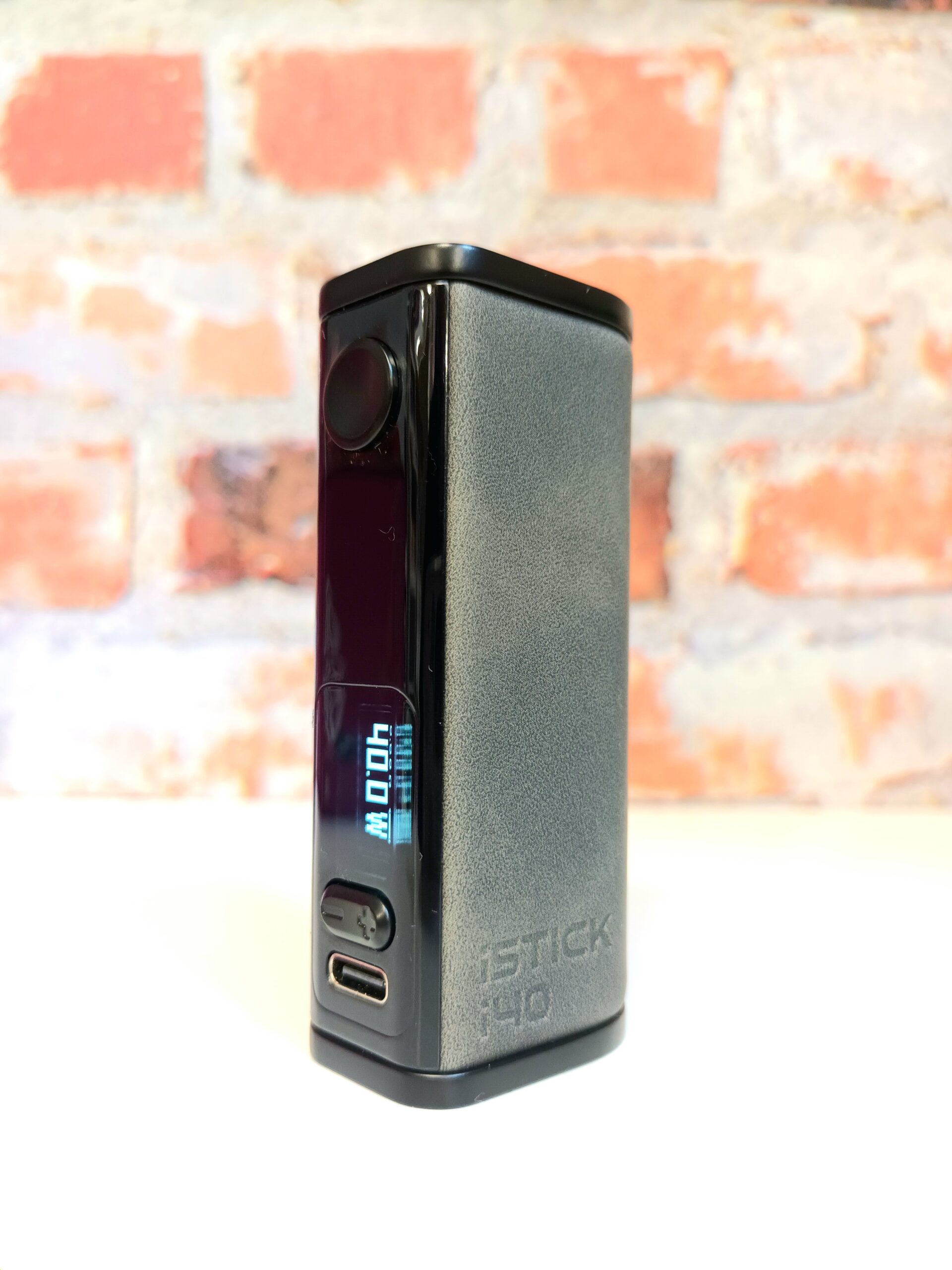 eLeaf iStick i40 mod with the screen on, standing on white shelf before a brick background